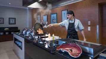 A chef cooking at a counter with a grill, steam rising, and a display case with plates.