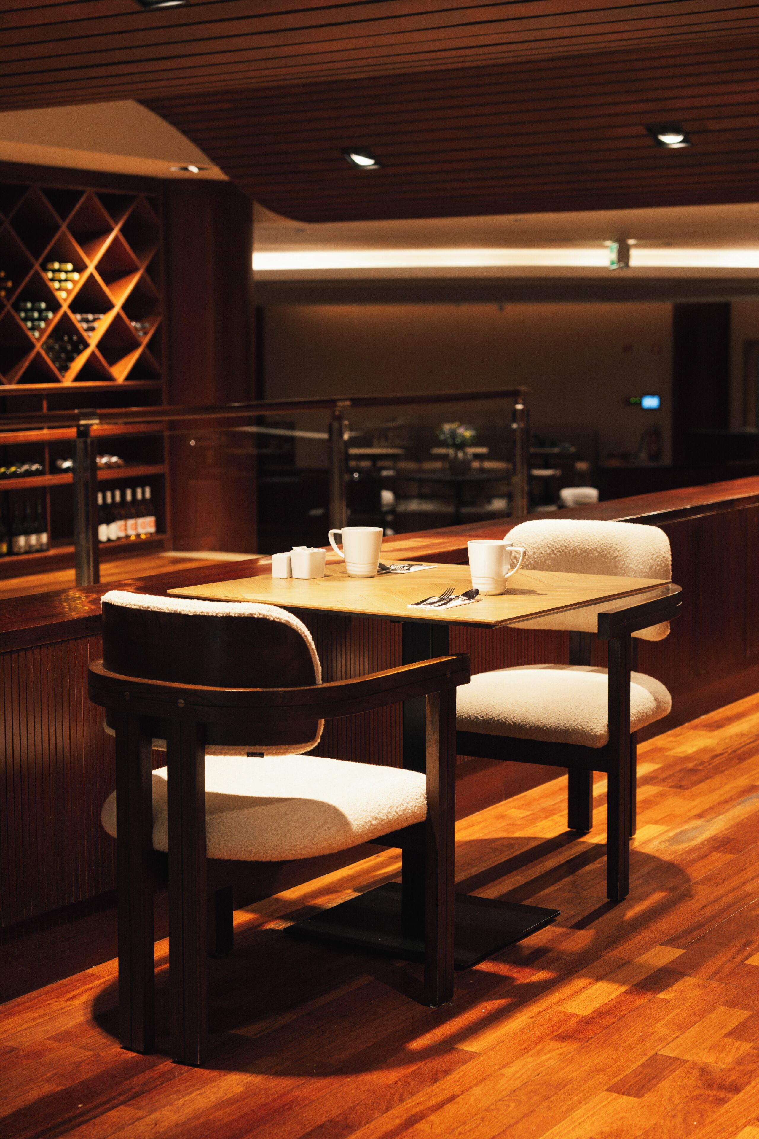 Eine Bar mit einem Holztisch, Stühlen und einem Weinkühlschrank im Hintergrund.