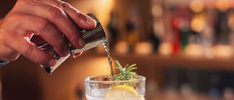 A hand pouring a drink into a glass with a lemon slice and a sprig of rosemary.