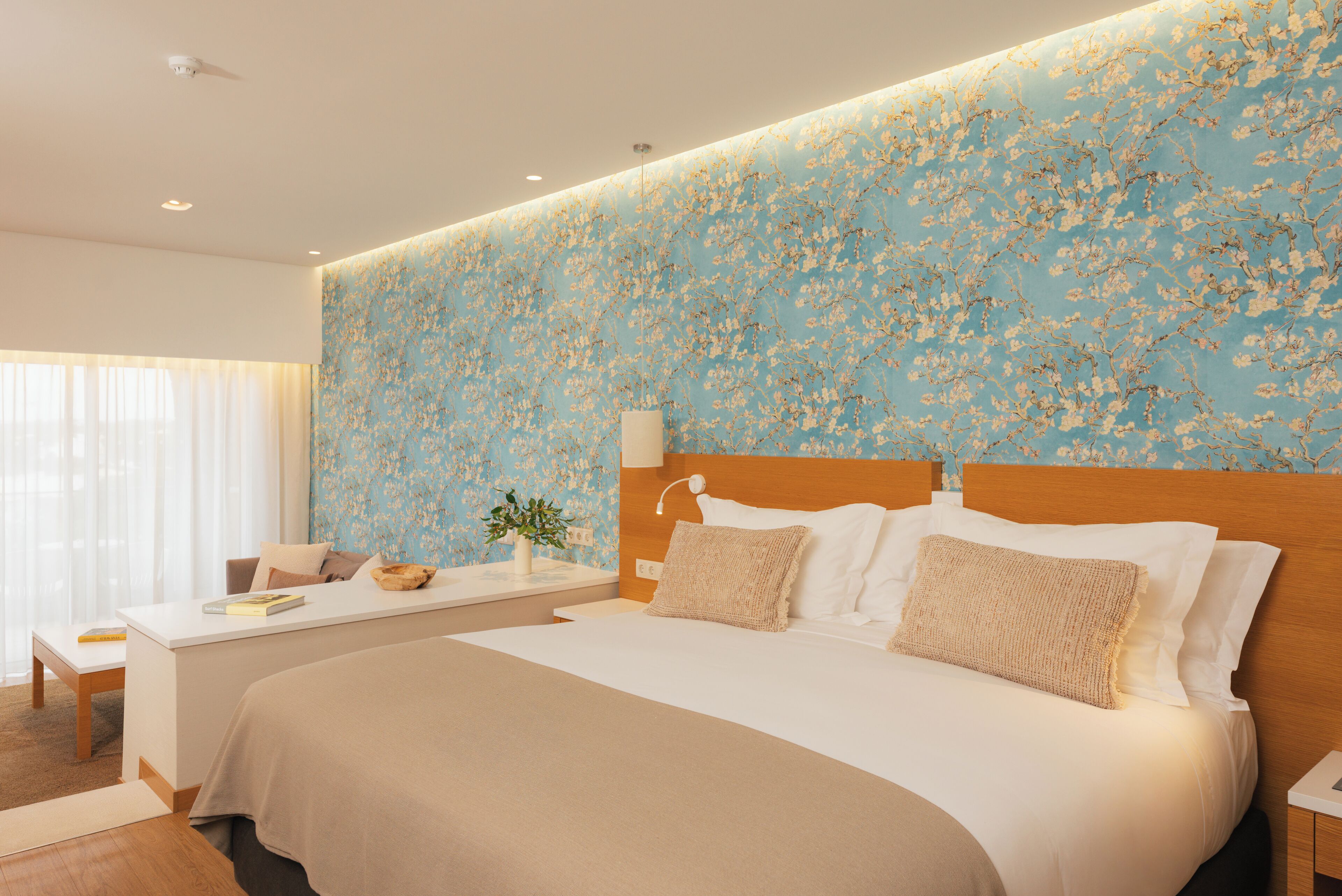 A hotel room with a large bed, a bedside table, a desk, and a window with curtains.
