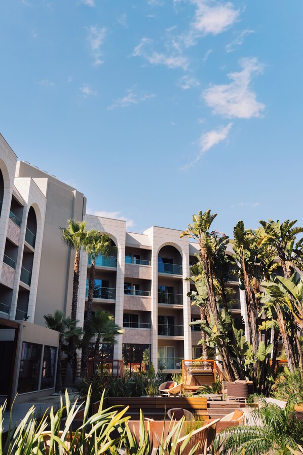 A hotel with multiple floors, outdoor seating, and palm trees. - Falésia Hotel - Adults Only (Albufeira)