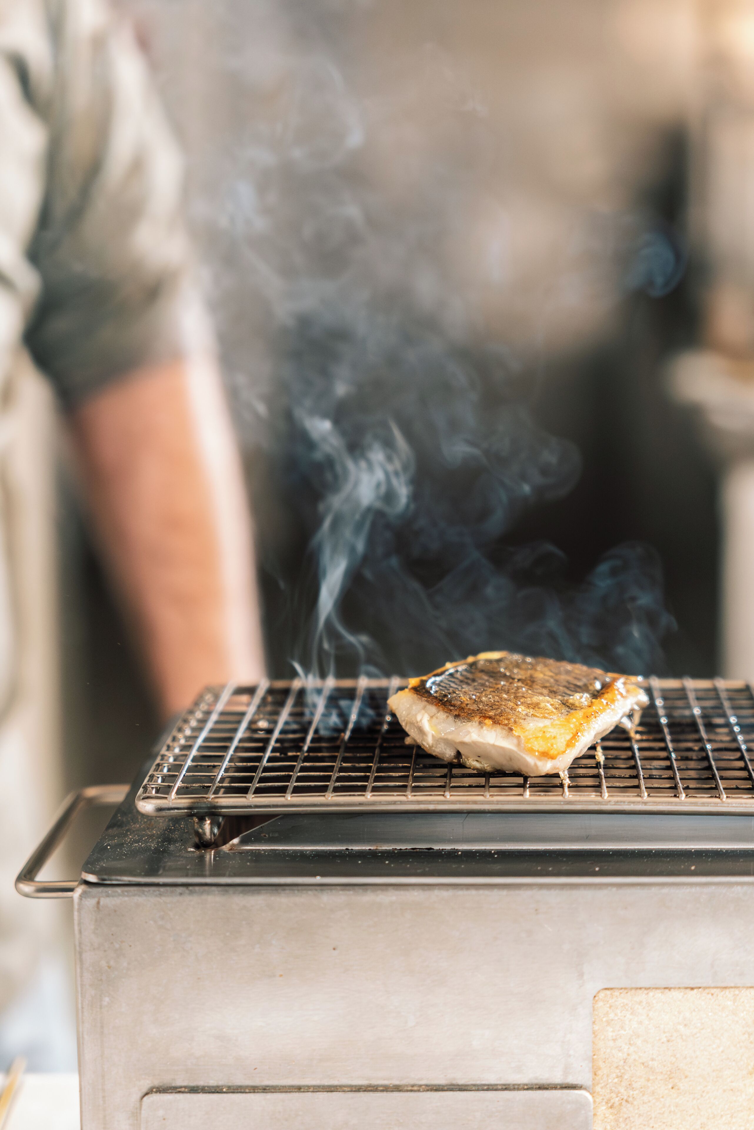 A grill with a piece of meat cooking, emitting smoke.