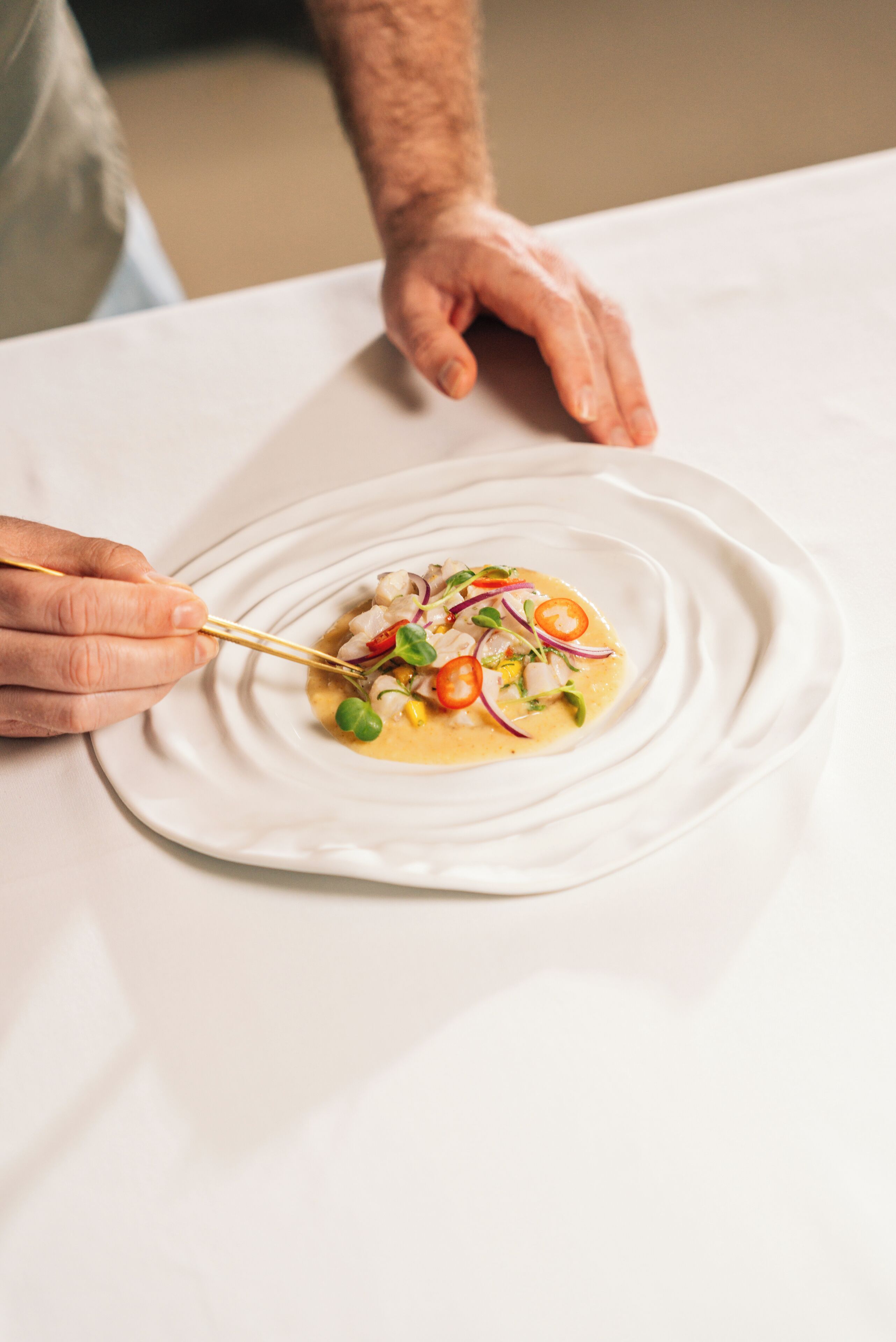 A person using chopsticks to eat a dish on a white plate.