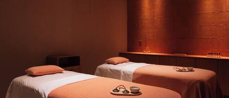 A room with two beds, a wooden wall, and a small table with a bowl and glasses.