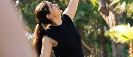 A person in a black outfit performing a yoga pose outdoors with trees in the background.