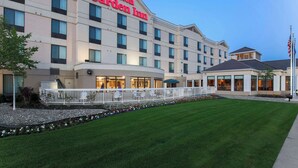 Un hotel Hilton Garden Inn amb una entrada espaiosa, un jardí ben cuidat i un alçapèrgol amb la bandera dels Estats Units.