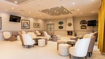 A spacious lounge area with multiple seating options, including sofas and chairs, arranged around a central fireplace.