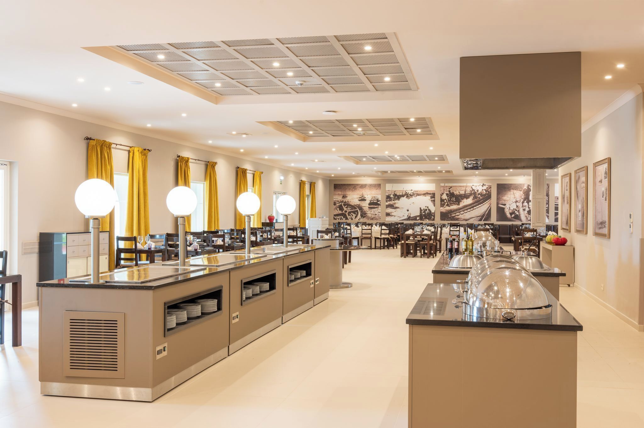 Une cuisine moderne dotée d’un îlot central, de luminaires suspendus et d’un coin repas avec chaises et tables.