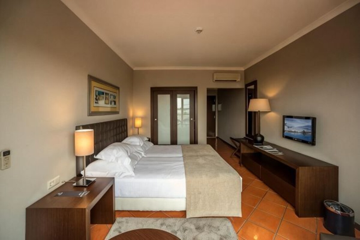 Une chambre d’hôtel comprenant un lit, des tables de chevet, une télévision et une porte donnant sur une autre pièce.