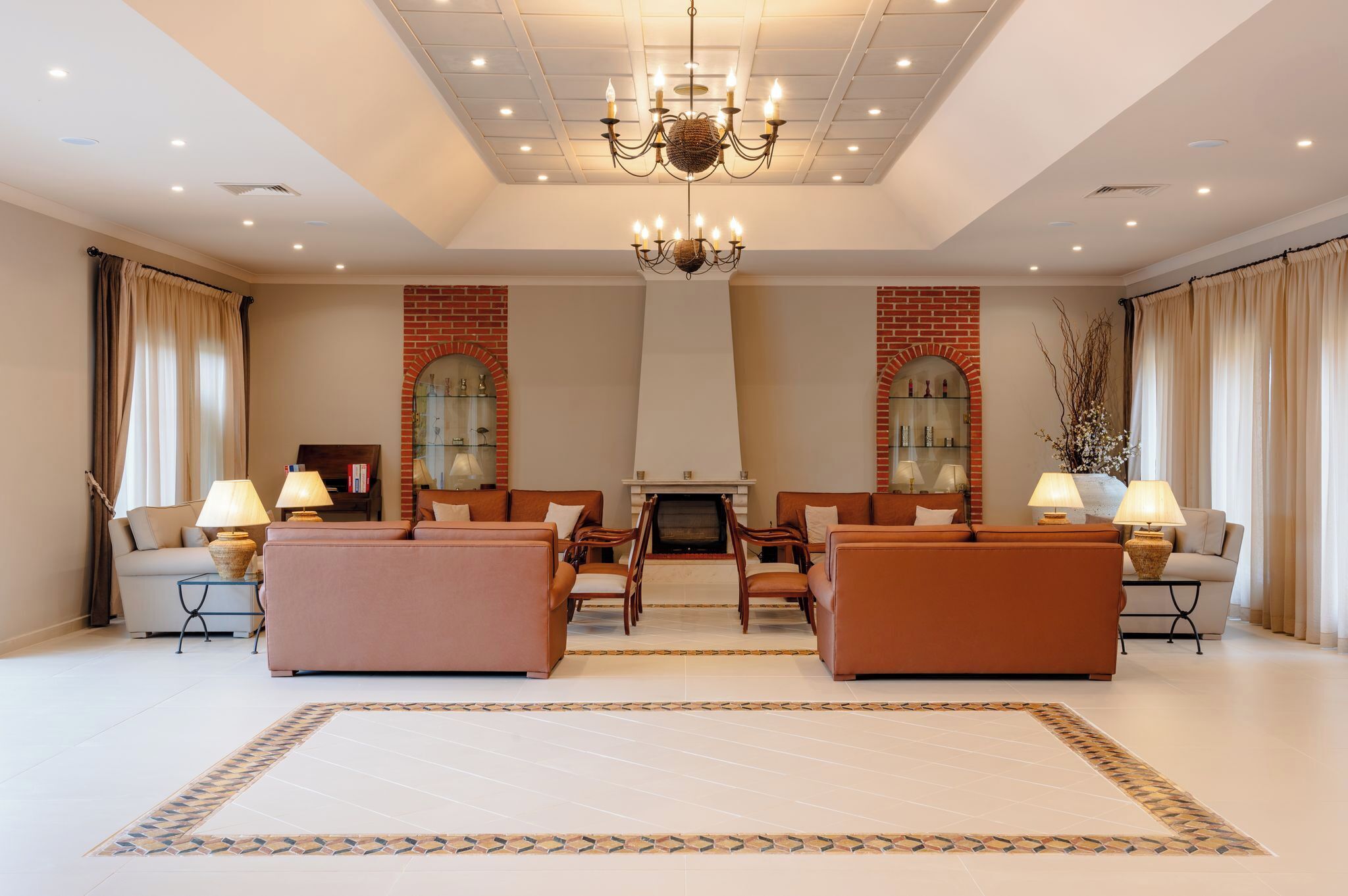 A spacious living room with a fireplace, two sofas, a chandelier, and a patterned rug.