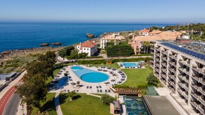 Un resort con múltiples piscinas, un edificio grande con balcones y vistas al mar.