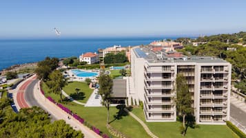 A coastal hotel with a swimming pool, a road curving around the property, and a view of the sea.
