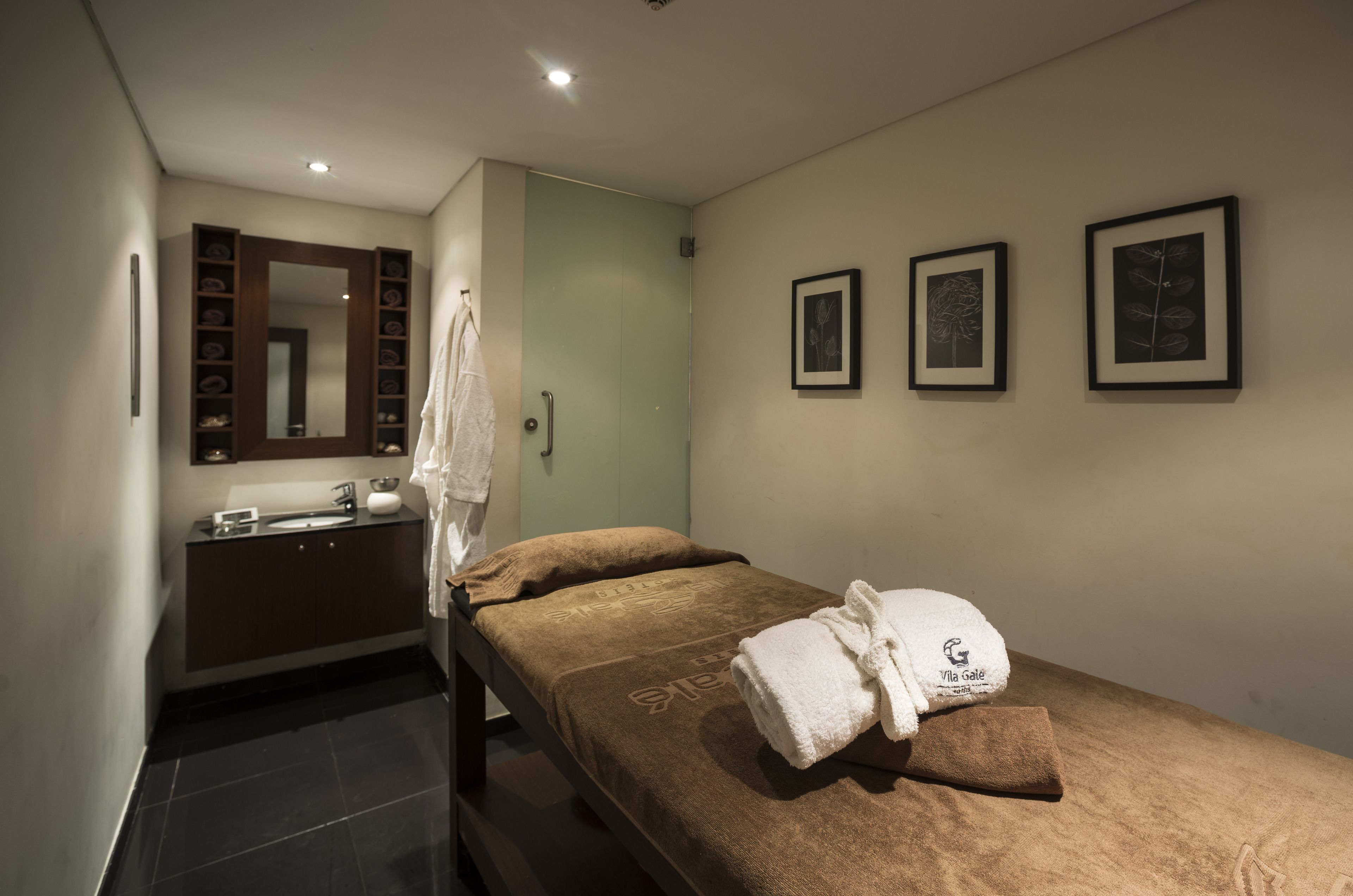 A hotel room with a bed, a bathroom with a mirror and shelves, and framed pictures on the wall.