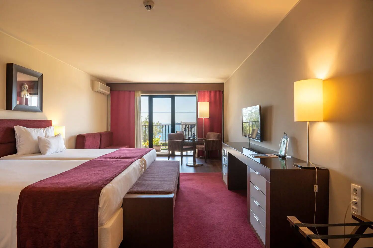 Habitación de hotel con dos camas, un escritorio, una silla, un televisor y un balcón con vistas.