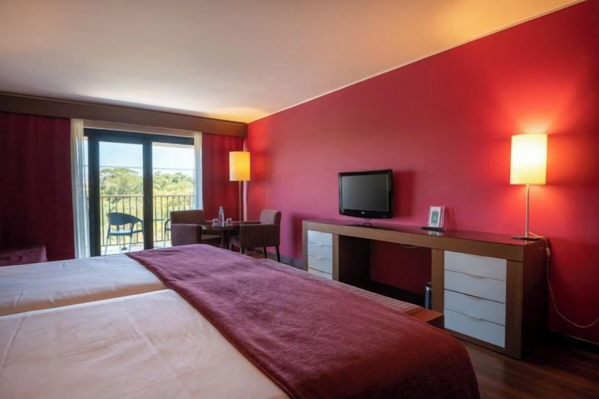 Habitación de hotel con dos camas, un escritorio, televisor y balcón.