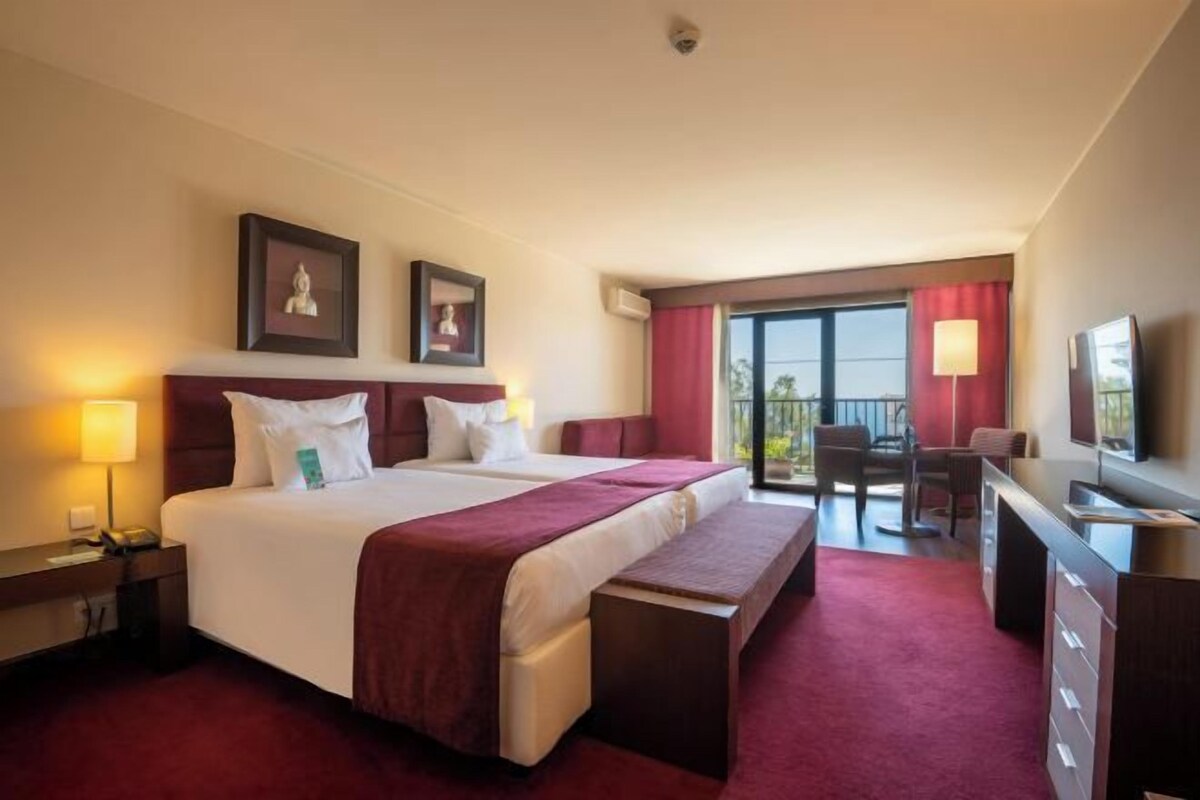 Habitación de hotel con una cama grande, un escritorio, una silla, un televisor y un balcón con vistas.