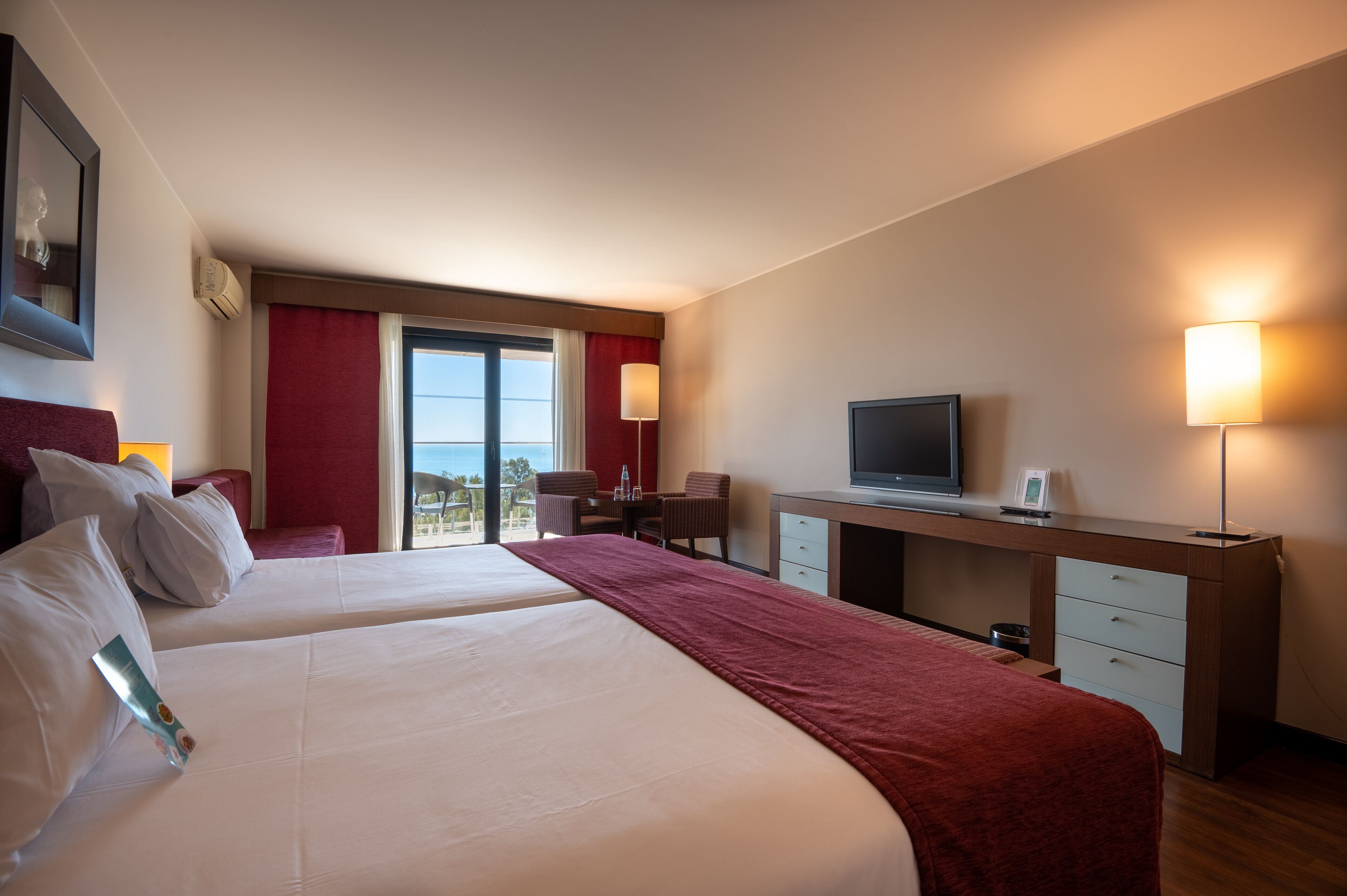 A hotel room with two beds, a desk with a television, and a view of the outdoors.