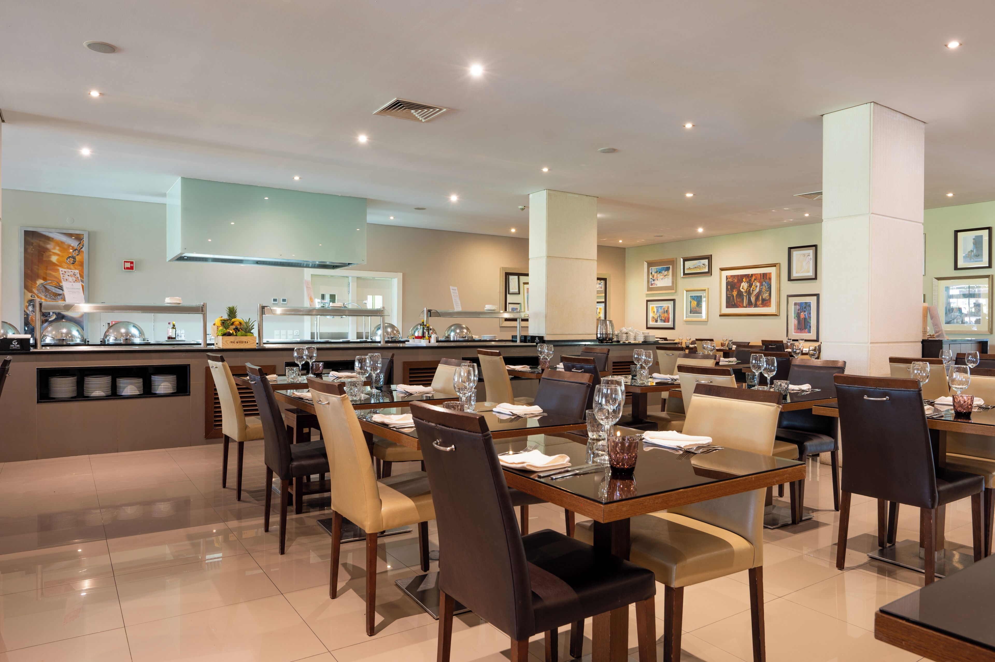 A modern dining area with multiple tables and chairs, a central counter with a display, and framed artwork on the walls.