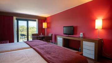 Habitación de hotel con dos camas, un escritorio, televisor y balcón con vistas.