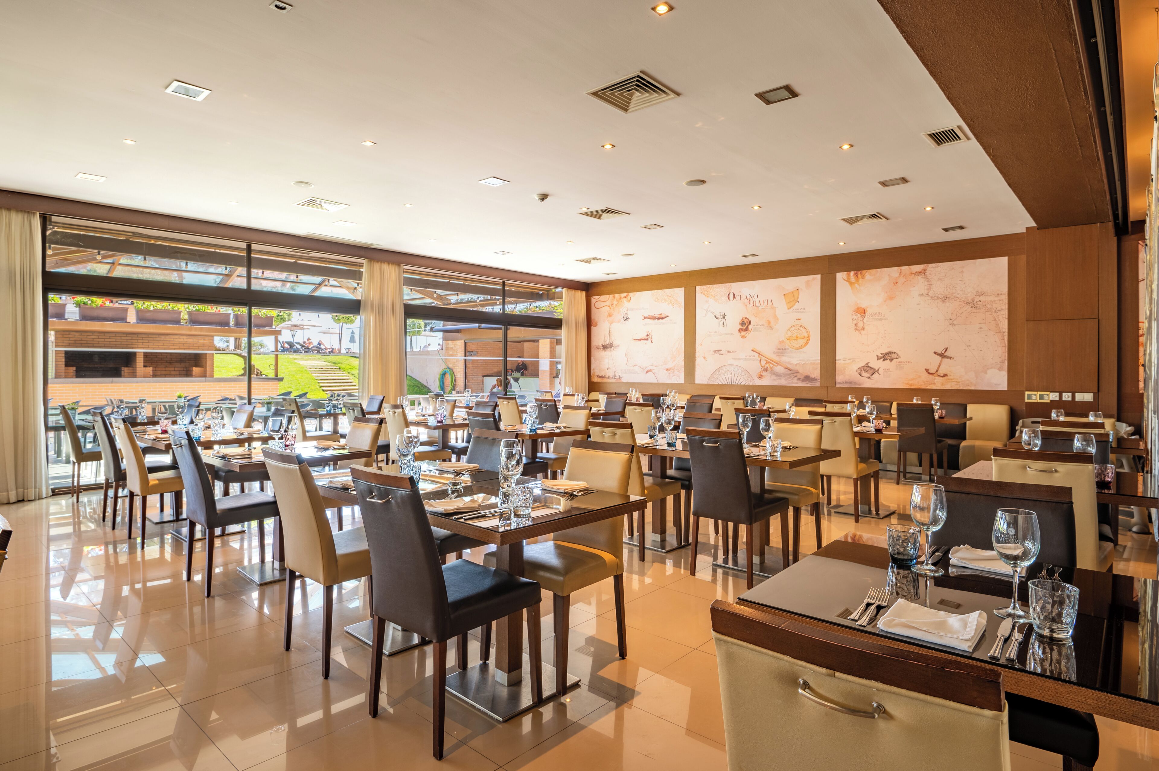 Un restaurant spacieux, doté de nombreuses tables et chaises, et de grandes fenêtres donnant sur l’espace extérieur aménagé pour les repas.