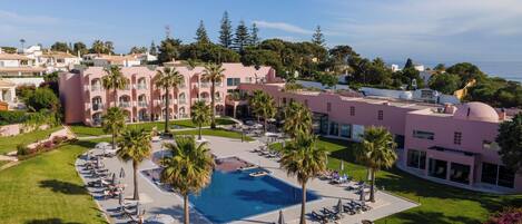 A resort with a swimming pool, lounge chairs, and a view of the sea.