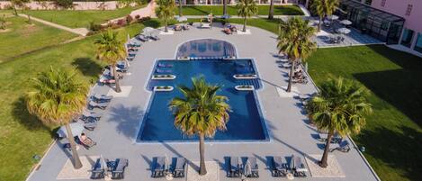 An aerial view of a resort with a central swimming pool, lounge areas, and palm trees.