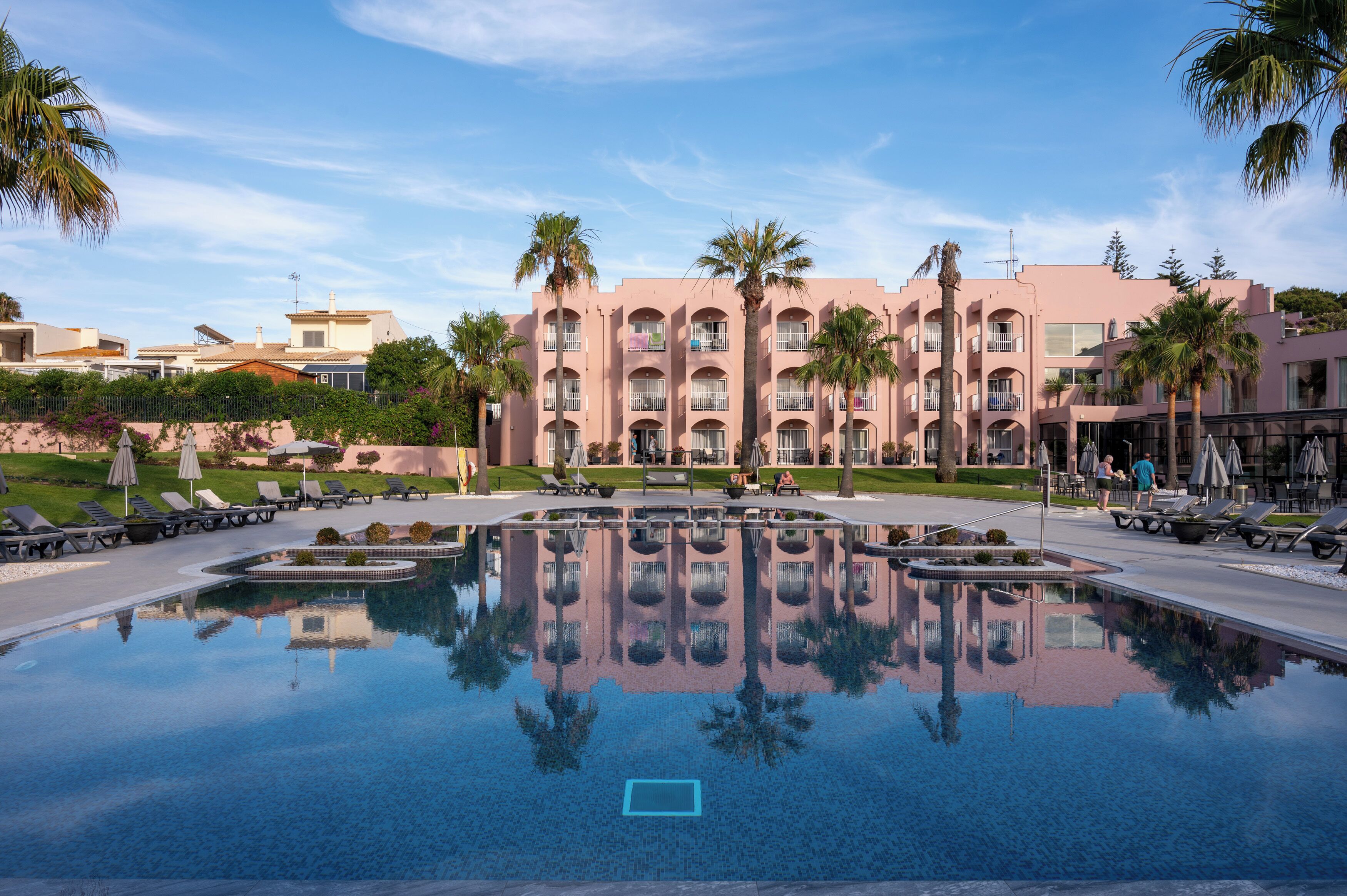 A hotel with a large reflective pool, palm trees, and a clear sky.