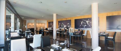 A modern restaurant with multiple dining tables and chairs, large columns, and artwork on the walls.