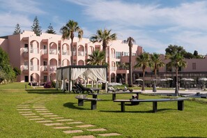 A hotel with a pink facade, outdoor seating, palm trees, and a clear sky. - Vila Gale Collection Praia Hotel (Albufeira)