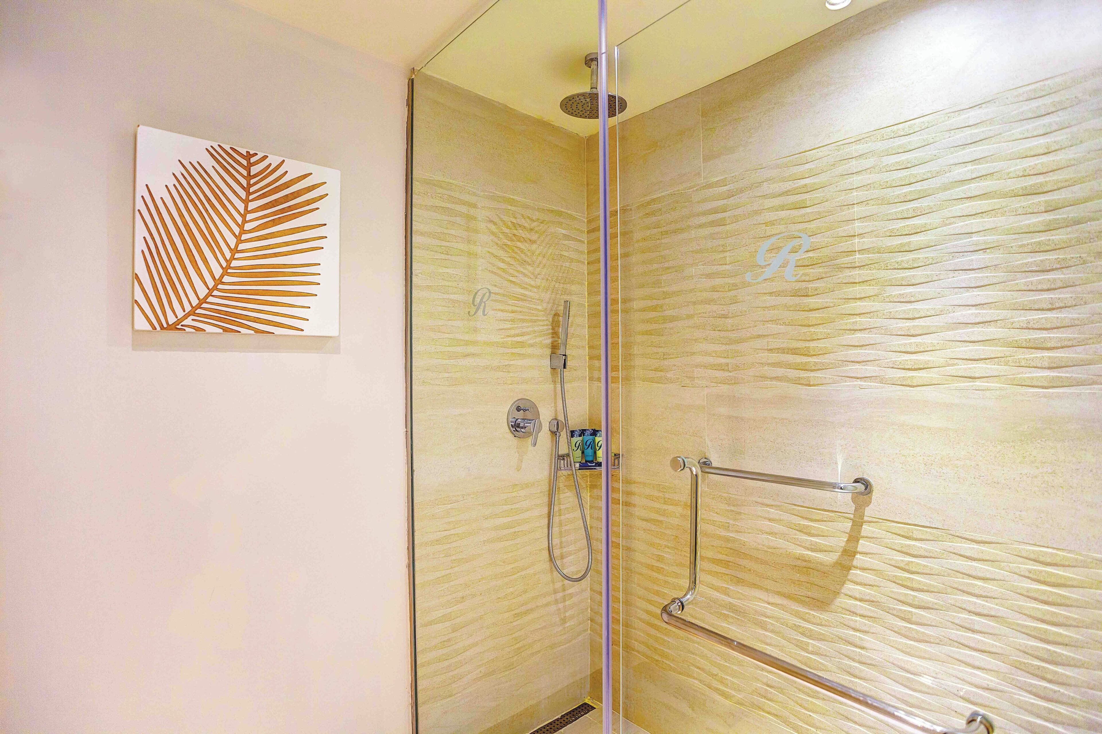 A glass-enclosed shower with a textured wall, a handrail, and a decorative leaf artwork on the adjacent wall.