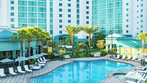 A hotel pool area with lounge chairs, umbrellas, and palm trees.