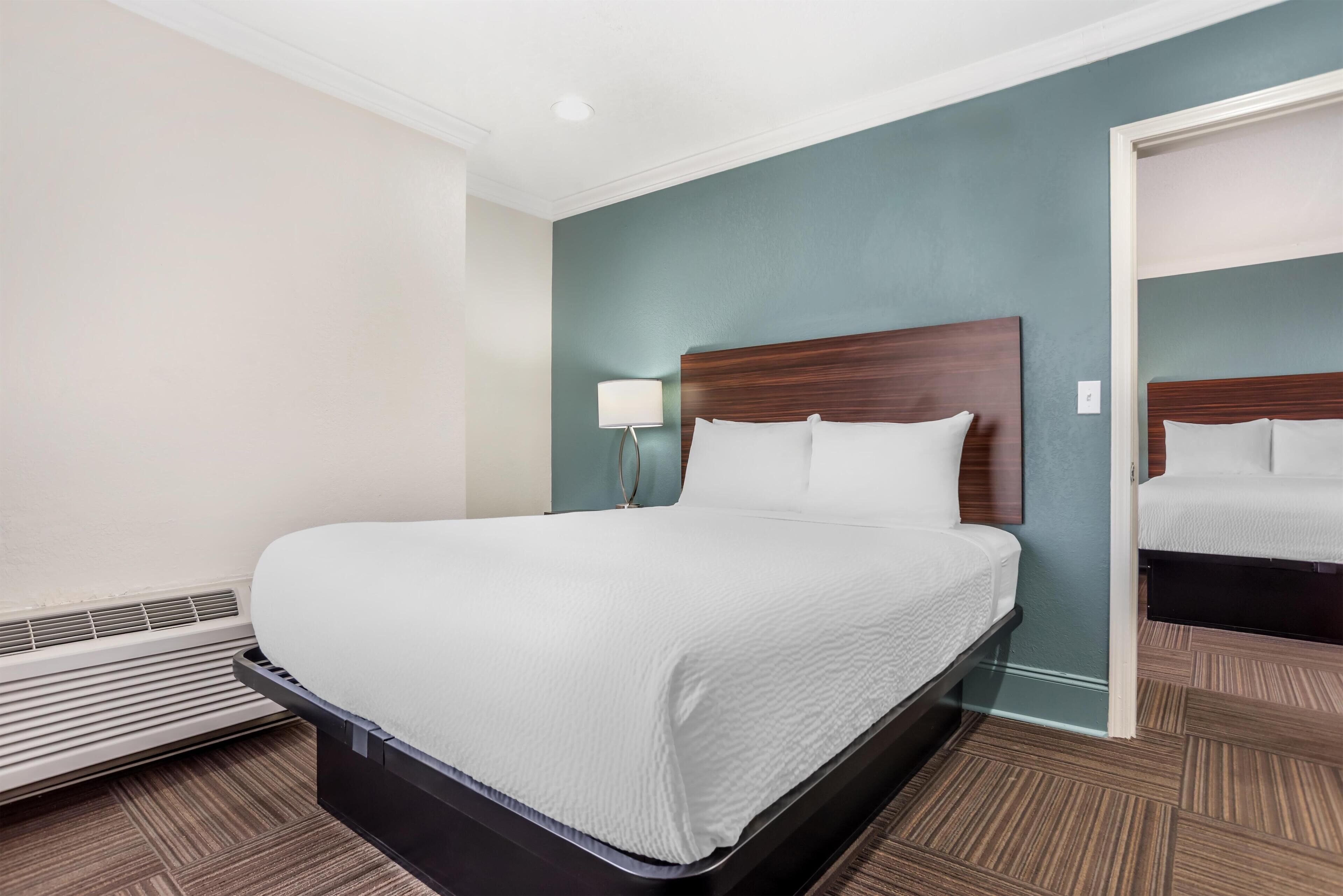A hotel room with a bed, a nightstand, a lamp, and a heater.