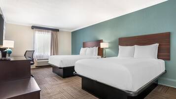 A hotel room with two beds, a desk, a chair, a lamp, and a window with curtains.