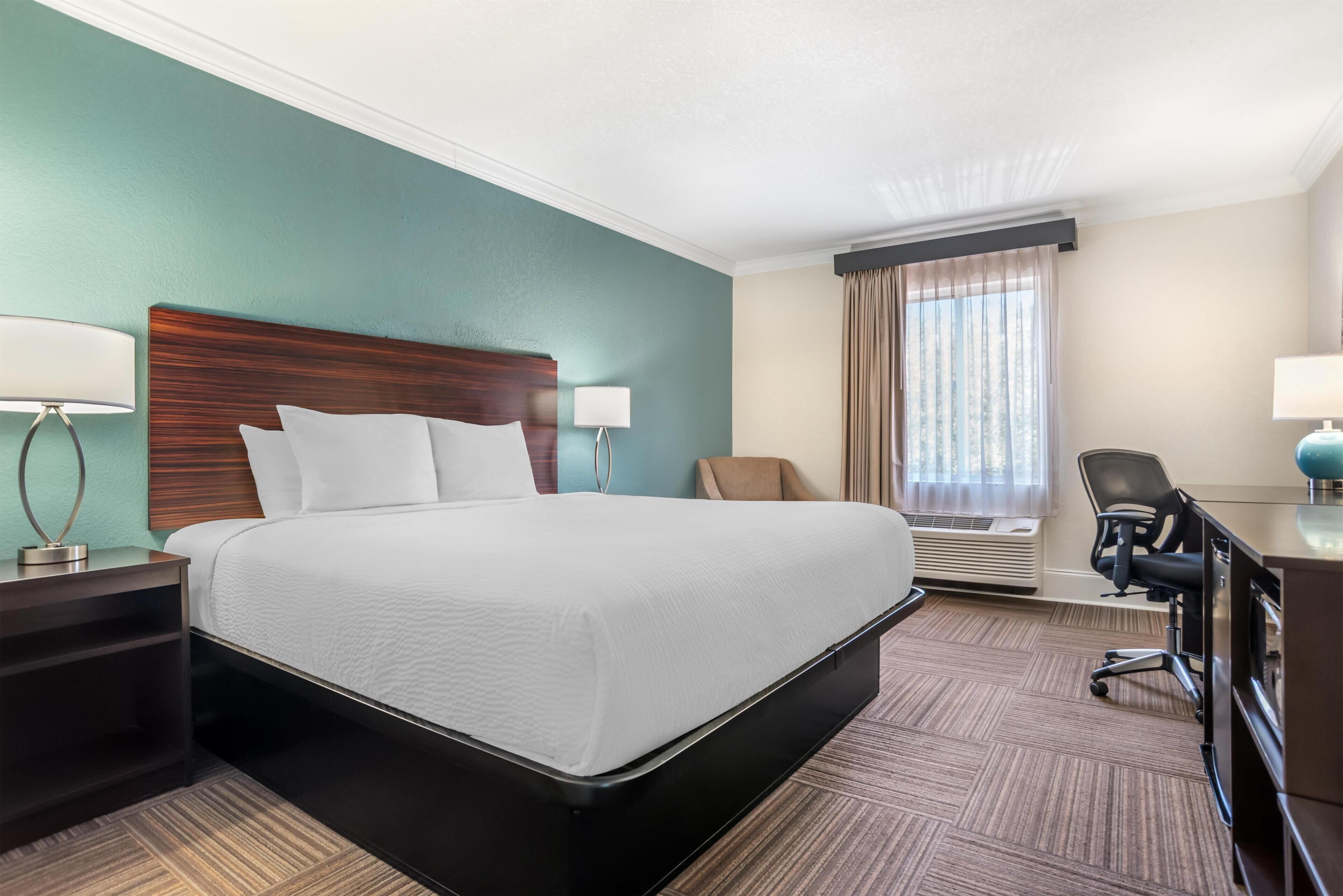 A hotel room with a large bed, a desk, a chair, and a window with curtains.