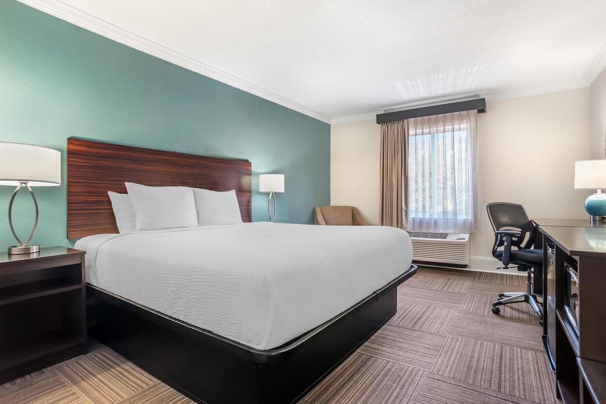 Una habitación de hotel con una cama grande, un escritorio, una silla y un ventanal con cortinas.