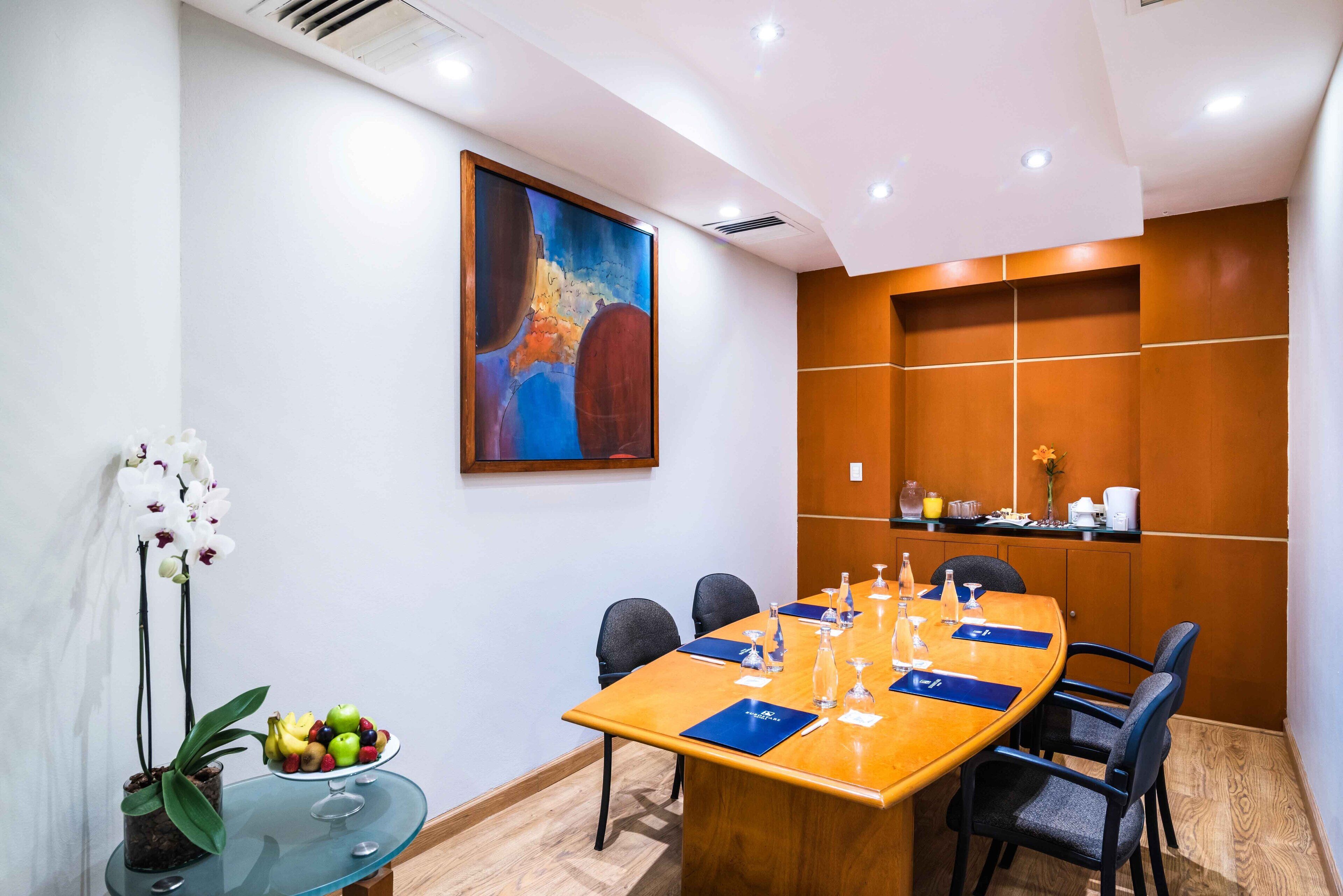 A conference room with a long table, chairs, a glass table with fruit, and a painting on the wall.