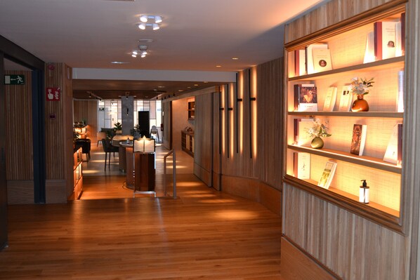 Un hall d’hôtel avec un plancher en bois, un comptoir de réception et un mur décoré de photos encadrées et d’un vase.