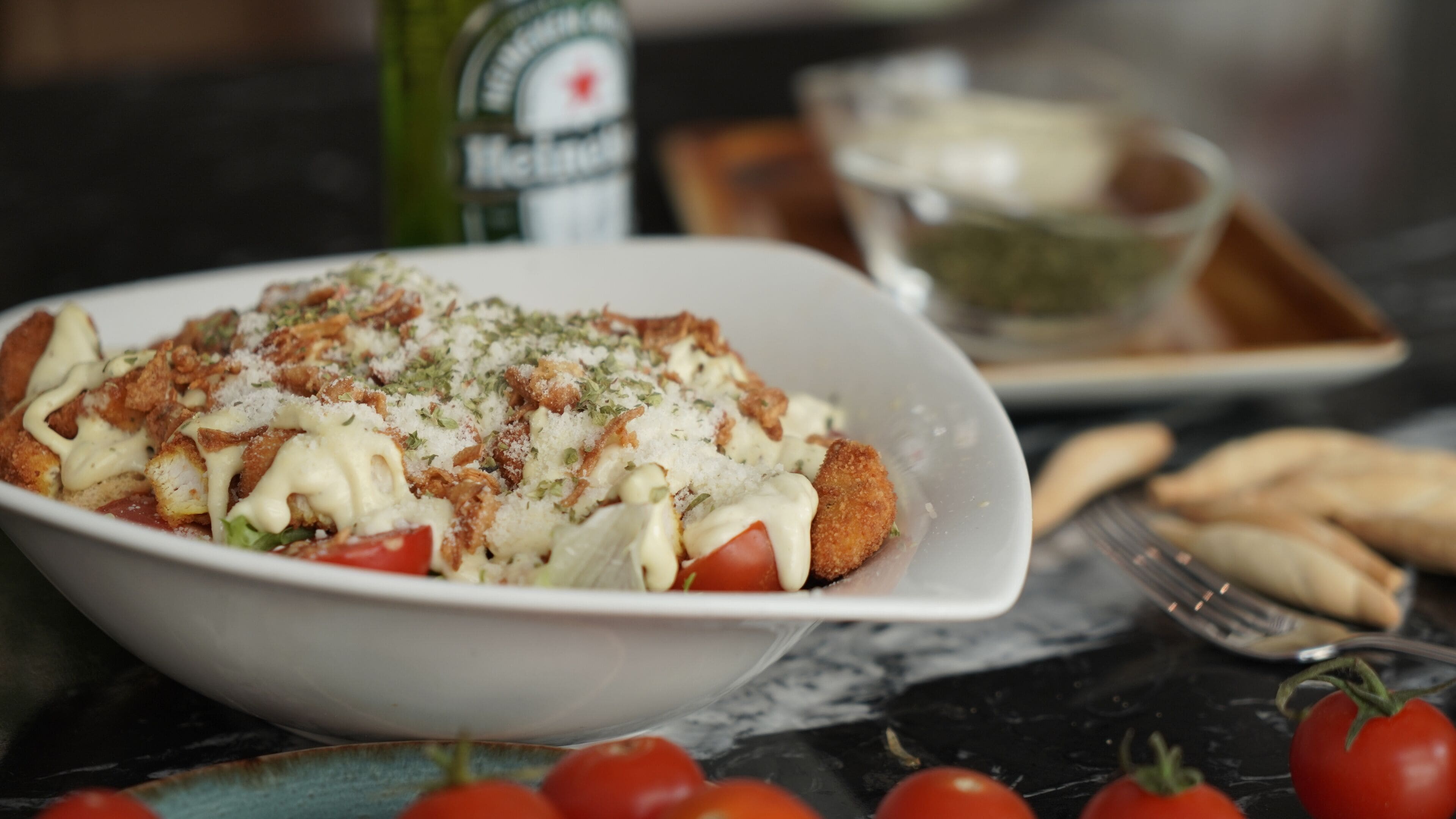 Un plato de comida con una fuente blanca, una botella y algunos tomates sobre una mesa.