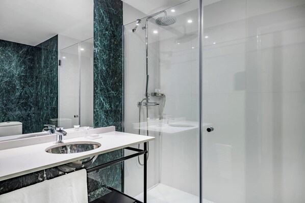 Un baño moderno con ducha de vidrio, un lavabo blanco y paredes de mármol.