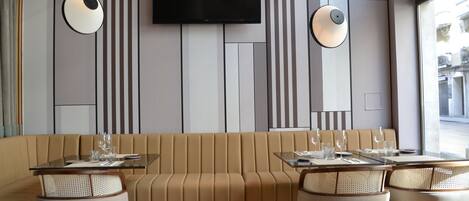 Un interior de restaurante moderno con una zona de asientos tipo banco corrido, mesas y un televisor de pantalla plana montado en la pared.
