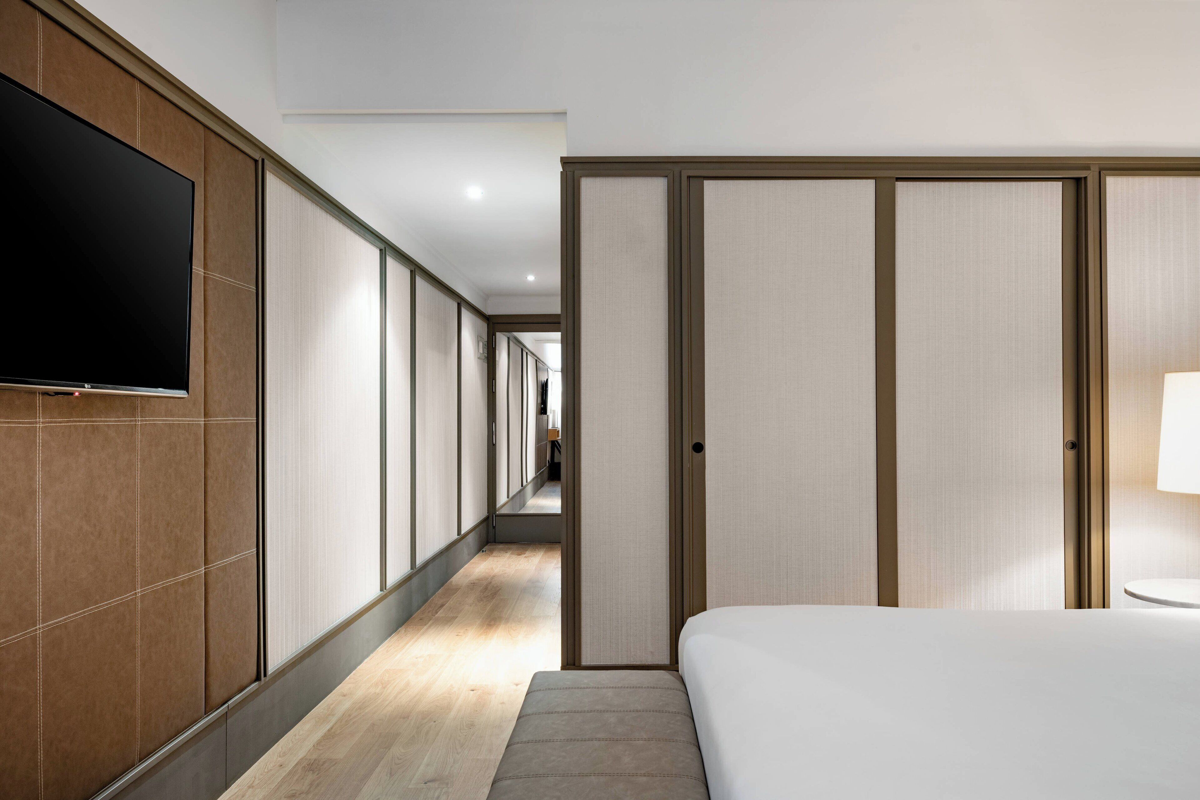 A hotel room with a large bed, a flat-screen TV mounted on the wall, a wooden floor, and sliding doors.