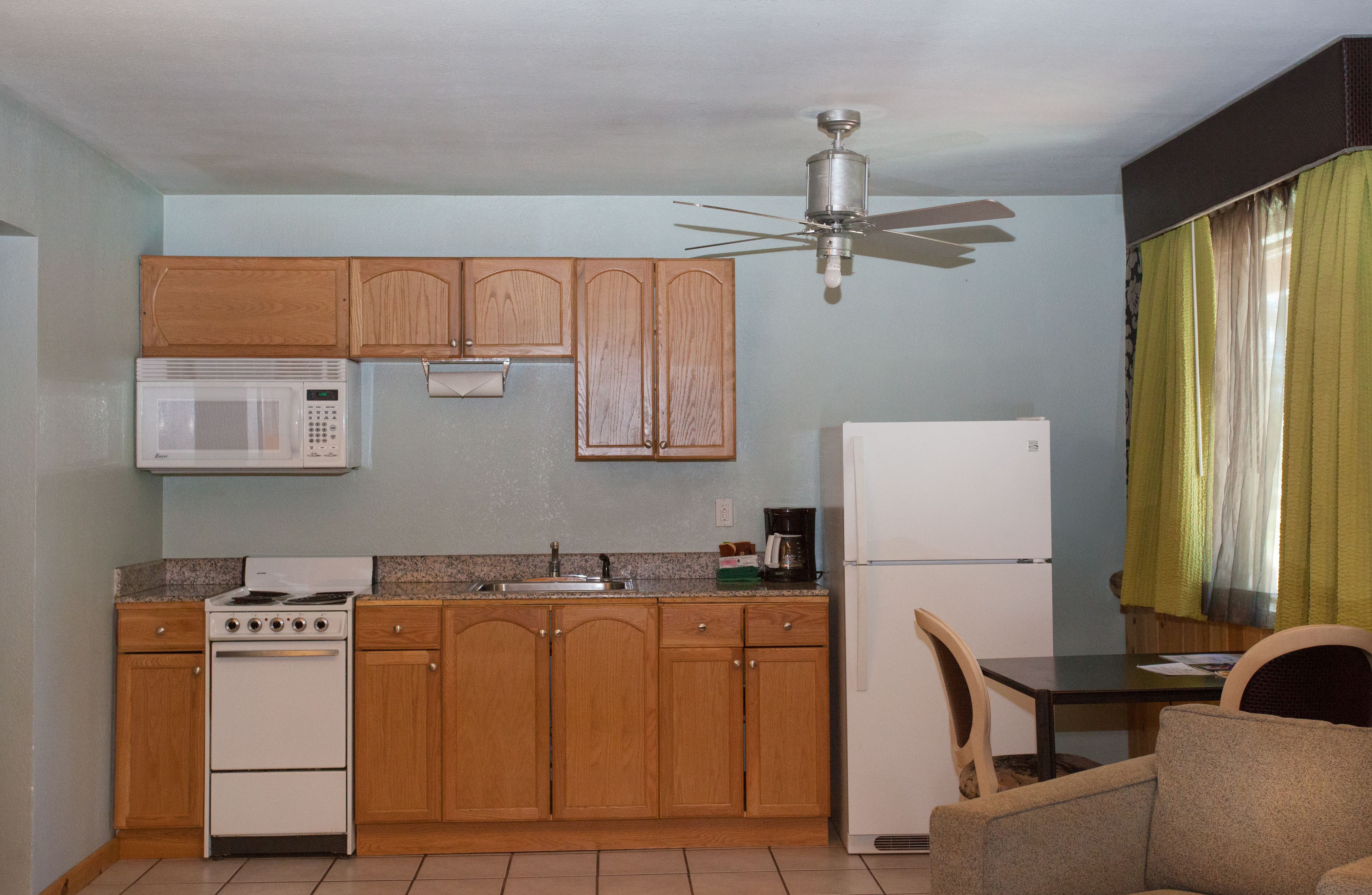 Une cuisine compacte dotée de meubles en bois, d’un four à micro-ondes, d’une cuisinière, d’un réfrigérateur et d’un ventilateur de plafond.
