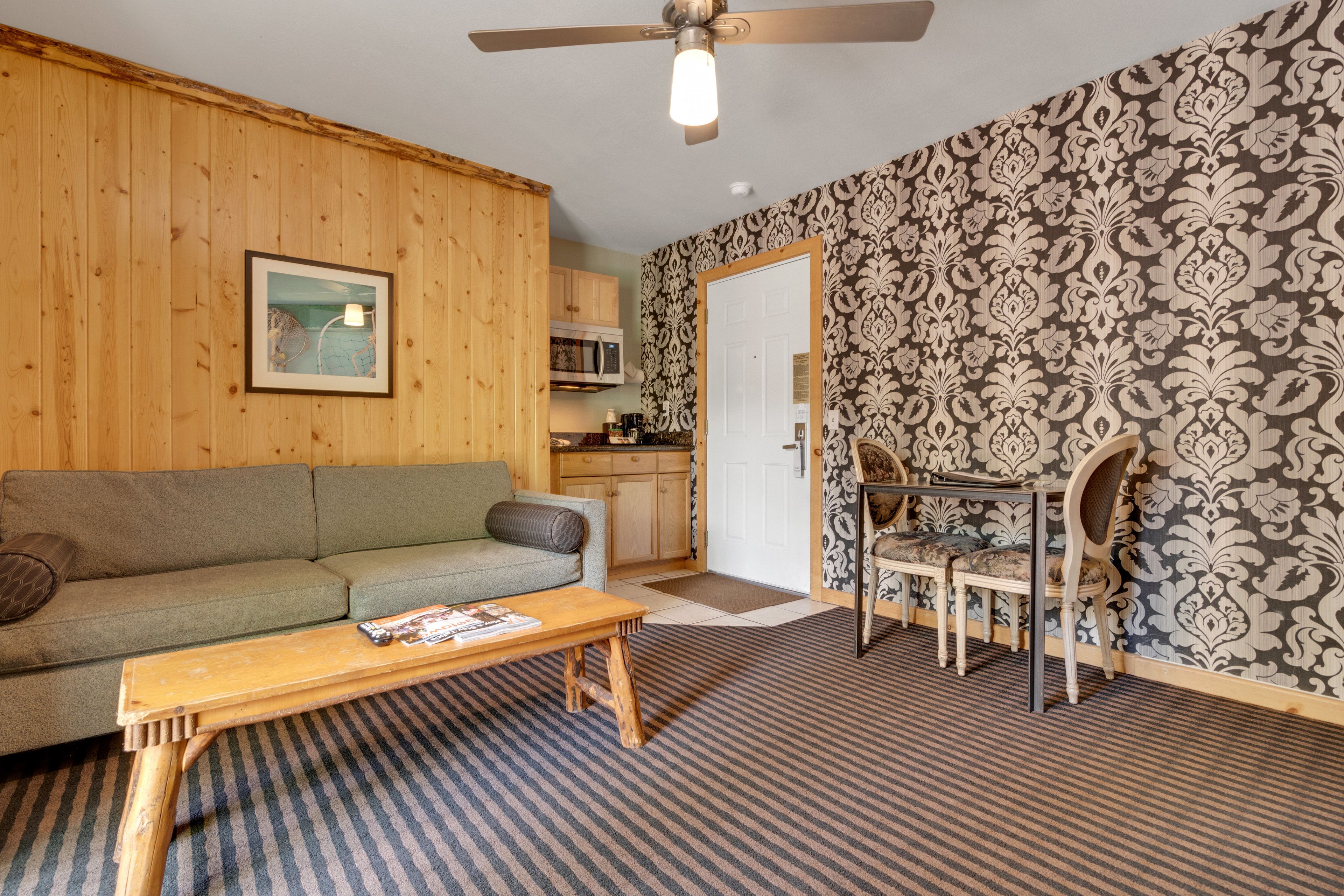 A cozy living room with a wooden ceiling fan, a green sofa, a wooden coffee table, and a patterned wallpaper.
