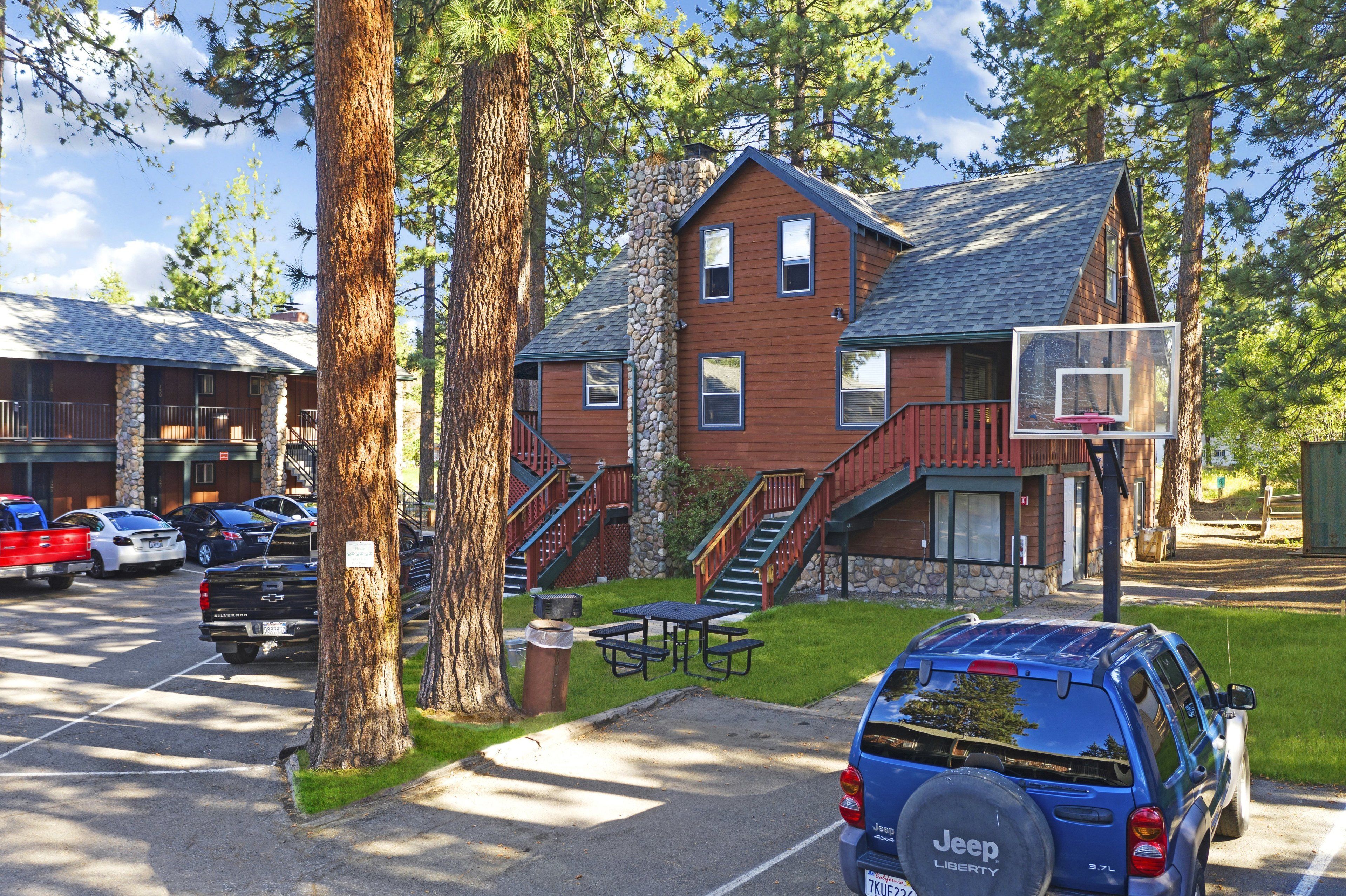 A lodge with a stone facade, a basketball court, and a parking area with several vehicles.