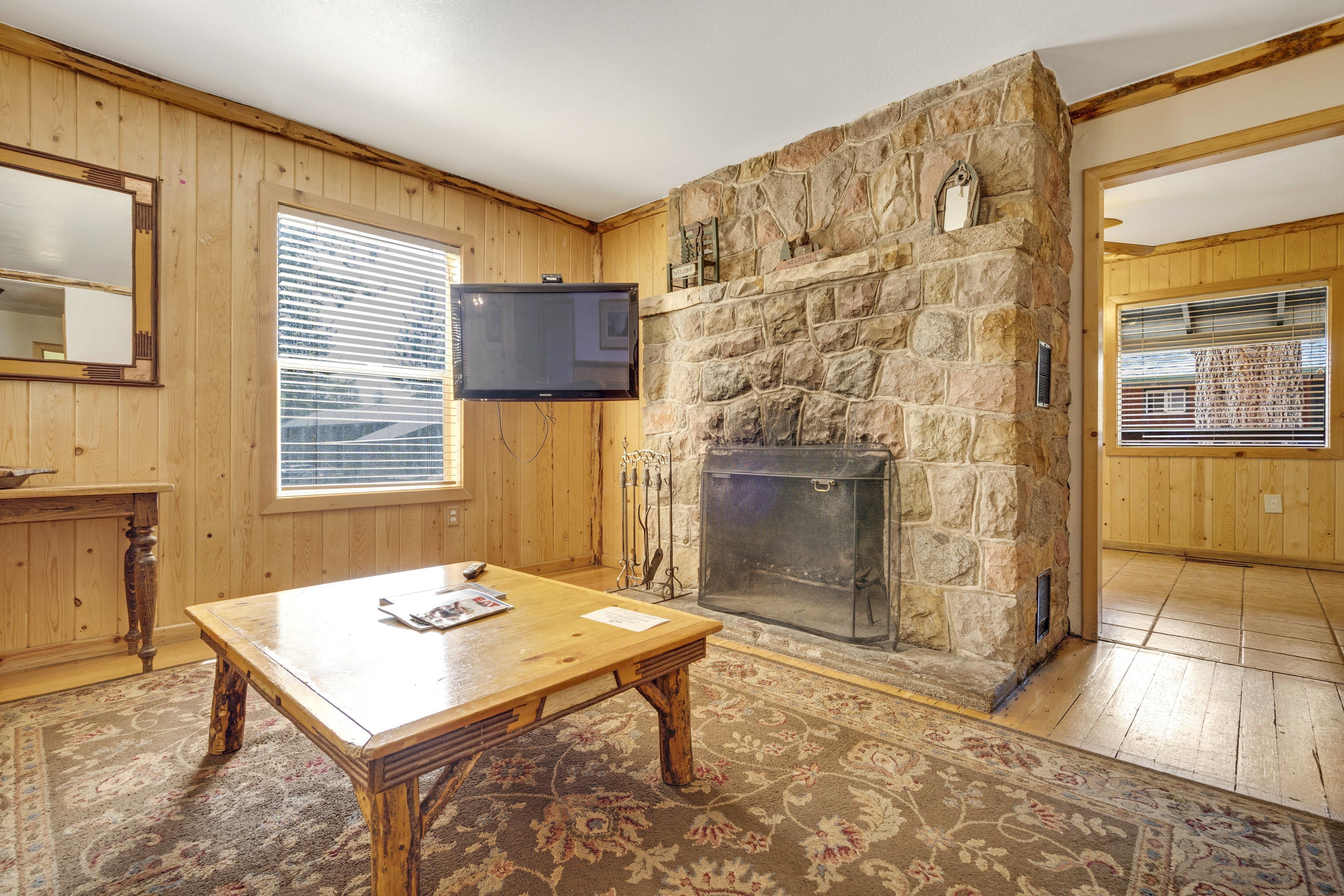 Una habitación con paneles de madera, chimenea de piedra y una mesa de madera.