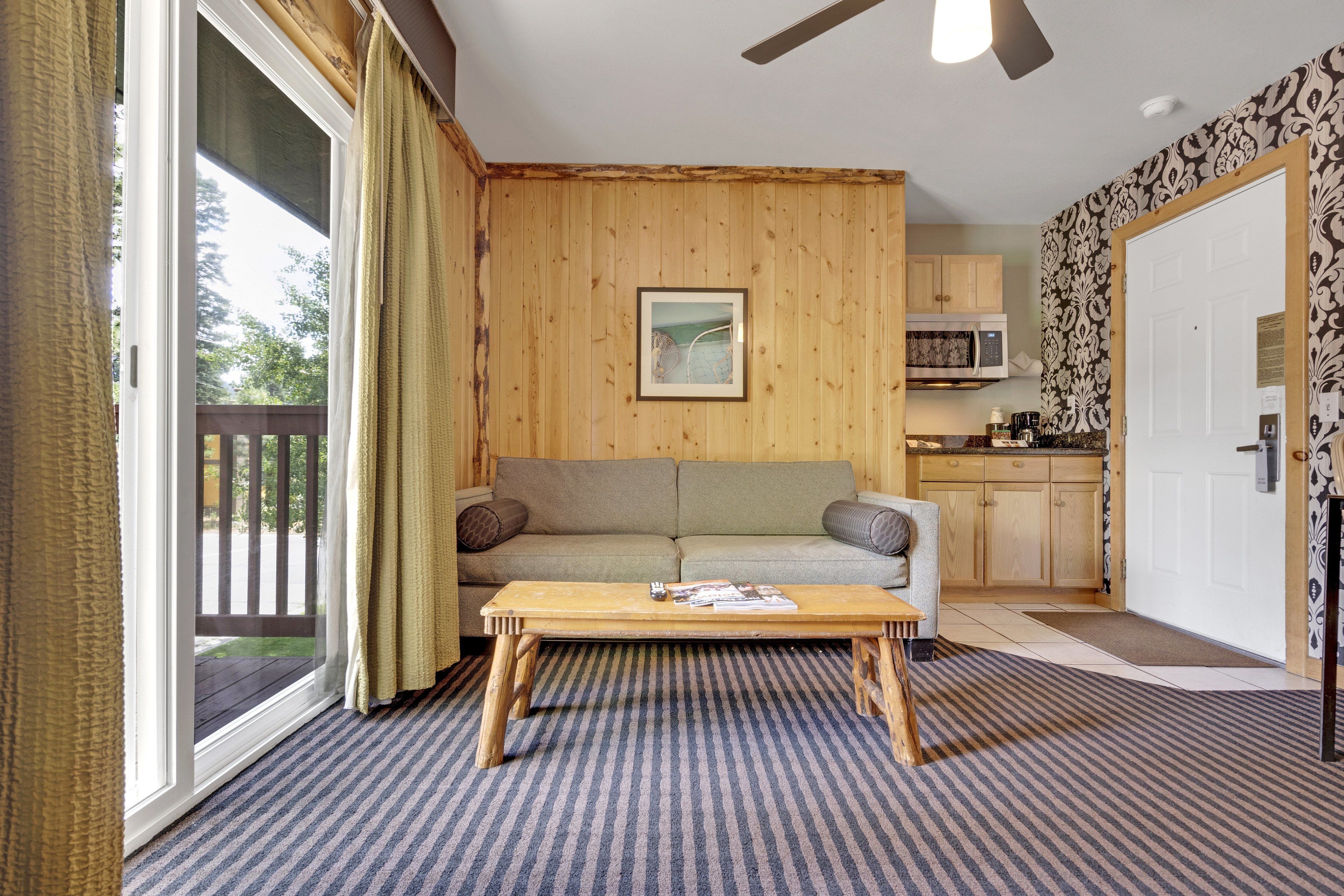 A cozy living room with a wooden floor, a sofa, a coffee table, and a view through a sliding glass door.