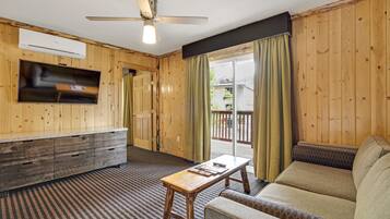 A room with a wooden interior, a ceiling fan, a flat-screen TV mounted on the wall, a sofa, a small table, and a sliding glass door leading to an outdoor area.