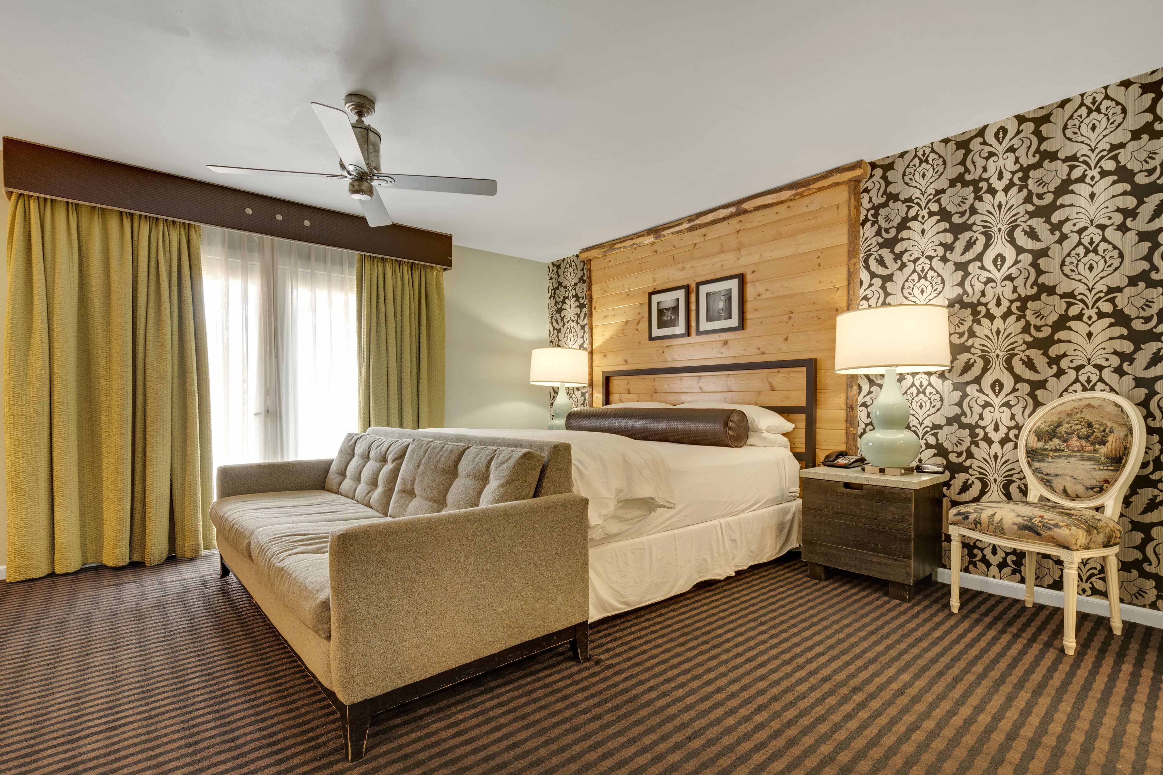 Een hotelkamer met een bed, een bank, een stoel, een nachtkastje, een lamp en een plafondventilator.