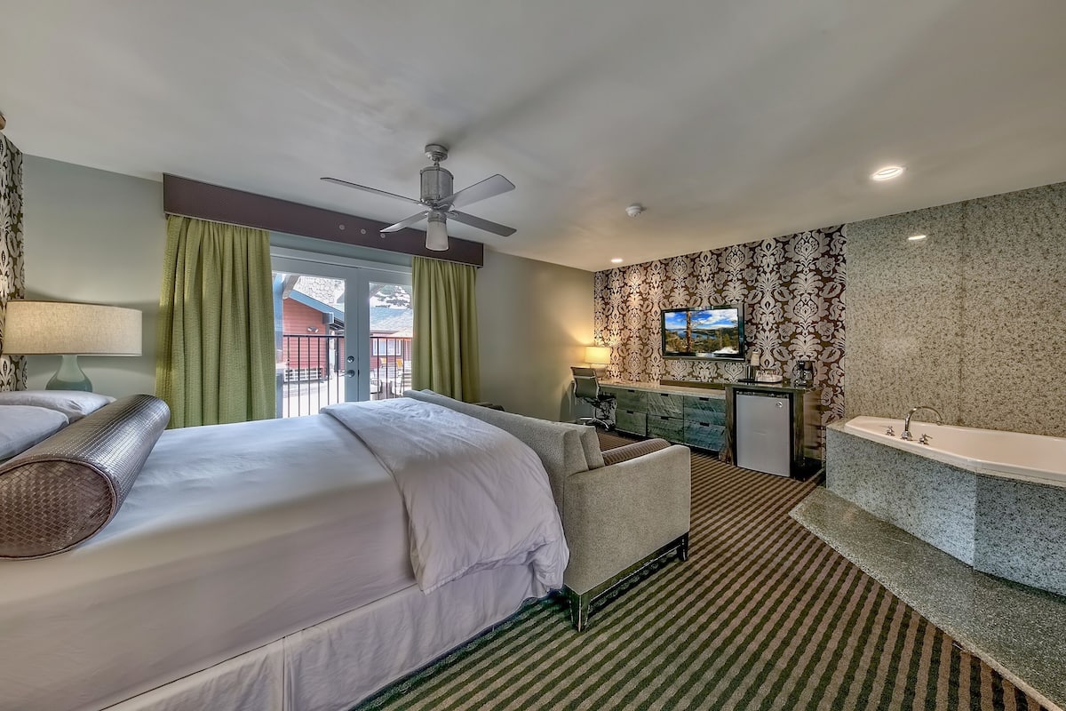 A hotel room with a bed, a sofa, a desk, a TV, a bathroom with a bathtub, and a window with curtains.