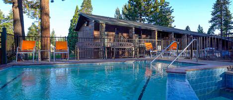 A pool area with a wooden building, outdoor seating, and a clear sky.